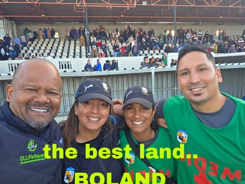 HealthPLUS medical team selfie in green medic vests at a Boland rugby stadium with spectators in the stands