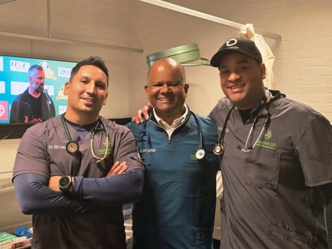 Three HealthPLUS doctors in scrubs in a clinic room; Dr Arthur Williams in the centre in teal scrubs